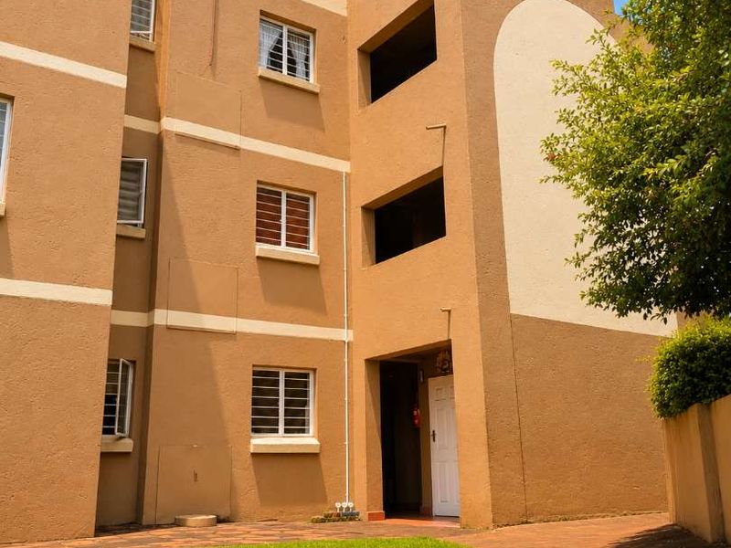 A view of the rear exterior of the townhouse complex, featuring a paved walkway, manicured lawn, and multi-story building facade.