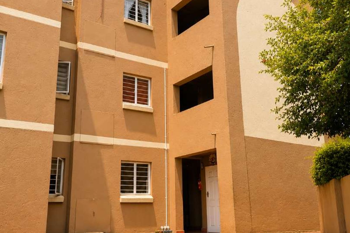 A view of the rear exterior of the townhouse complex, featuring a paved walkway, manicured lawn, and multi-story building facade.