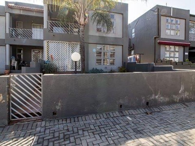 Front view of a multi-story apartment complex featuring grey exterior walls, private balconies, and a paved entrance area with a gated boundary wall.