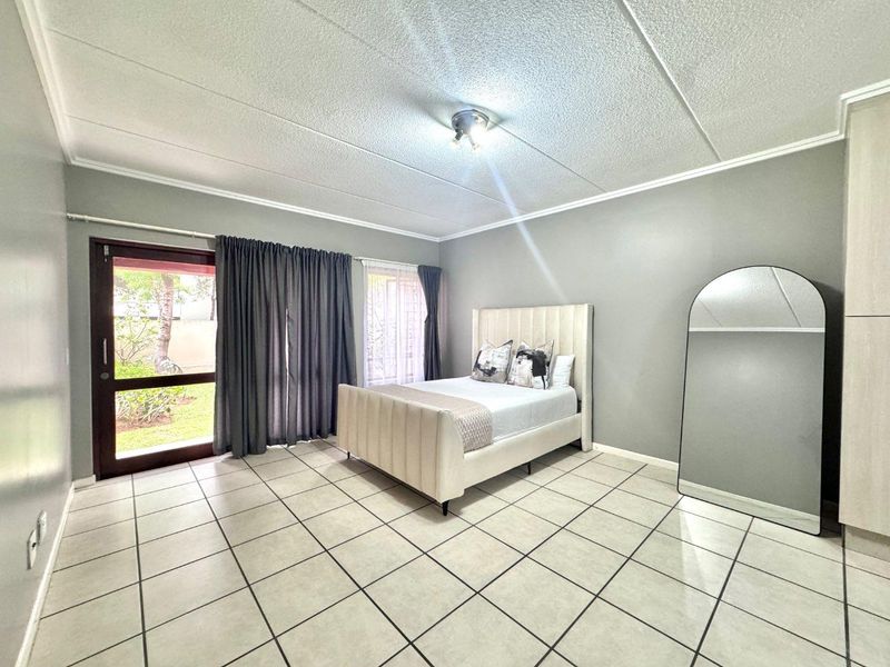 Spacious bedroom featuring tiled flooring, a drop ceiling, and direct access to the garden through a glass sliding door.