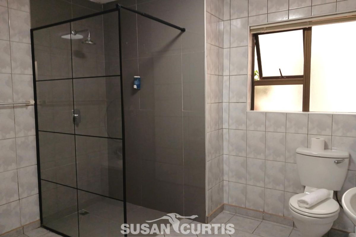 A modern bathroom featuring a walk-in shower with a black-framed glass enclosure, tiled walls, and a standard toilet.
