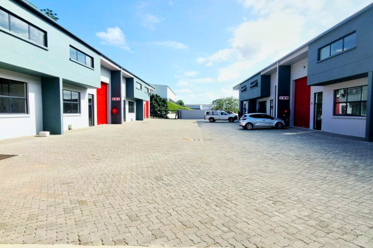 A modern industrial complex featuring paved courtyard access, multiple roller shutter doors, and contemporary facade finishes.