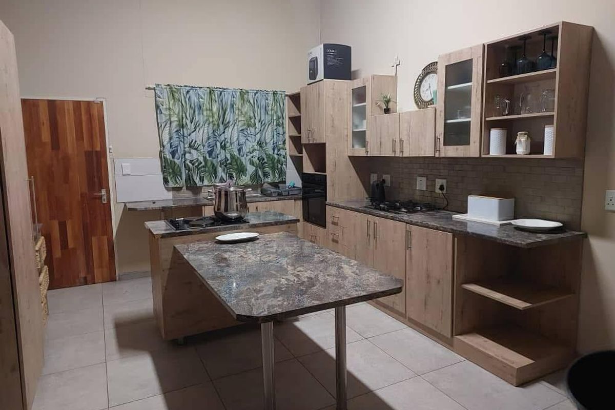 A functional kitchen featuring light wood-tone cabinetry, stone-look countertops, a central island, and built-in cooking appliances with tiled flooring.