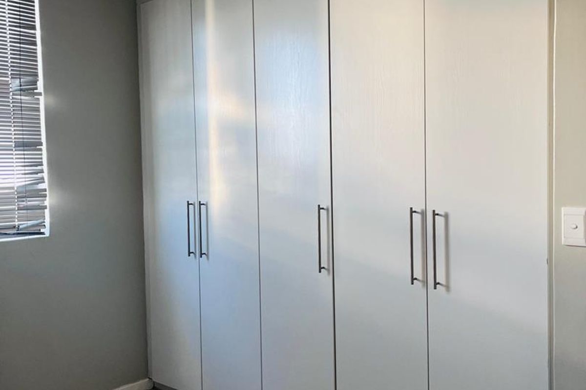 A bedroom featuring floor-to-ceiling built-in wardrobes with modern handles, tiled flooring, and a window with fitted blinds.