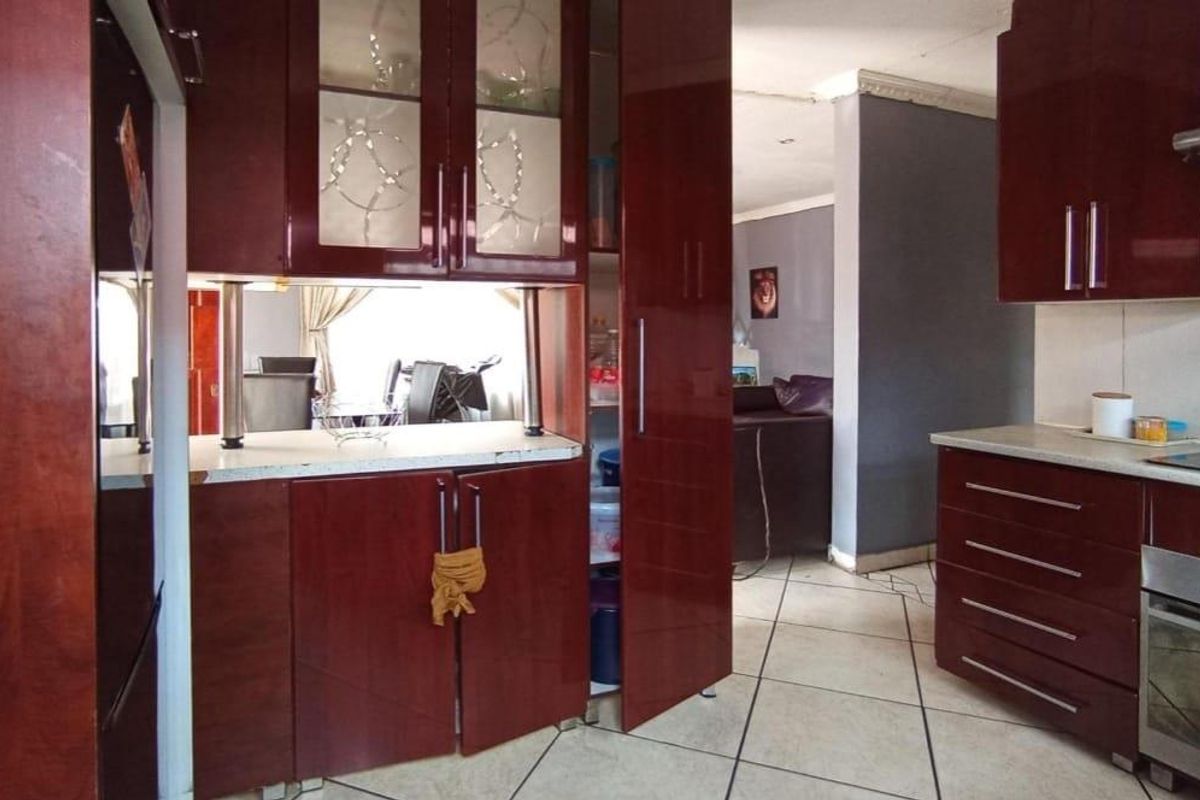 A functional kitchen featuring dark wood-finish cabinetry, built-in oven, hob, and extractor fan, with tiled flooring and a pass-through window to the living area.