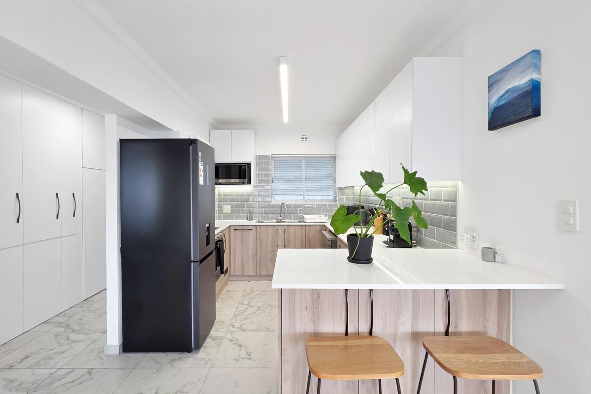 Modern kitchen featuring sleek white and wood-tone cabinetry, stone countertops, a subway tile backsplash, and a functional breakfast bar with marble-look flooring.