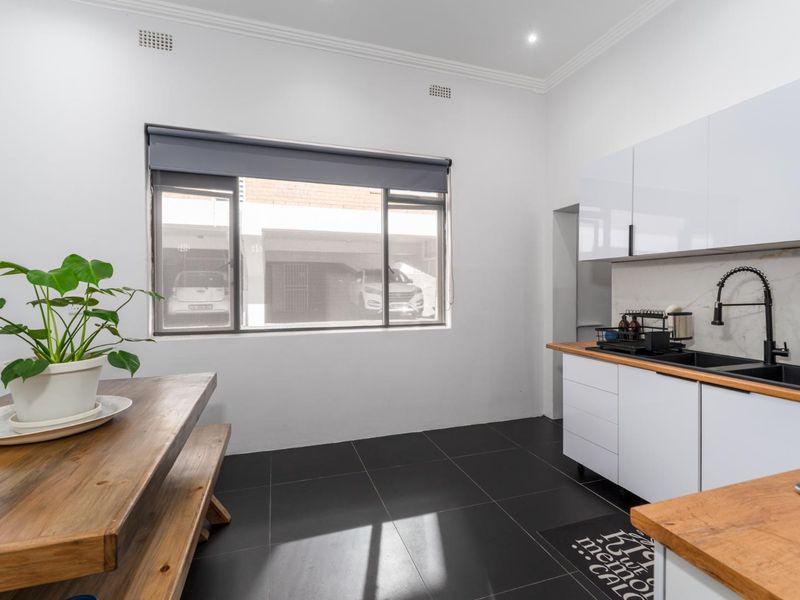 Modern kitchen featuring white gloss cabinetry, wooden countertops, a black double sink with a gooseneck faucet, and stylish marble-look splashback.