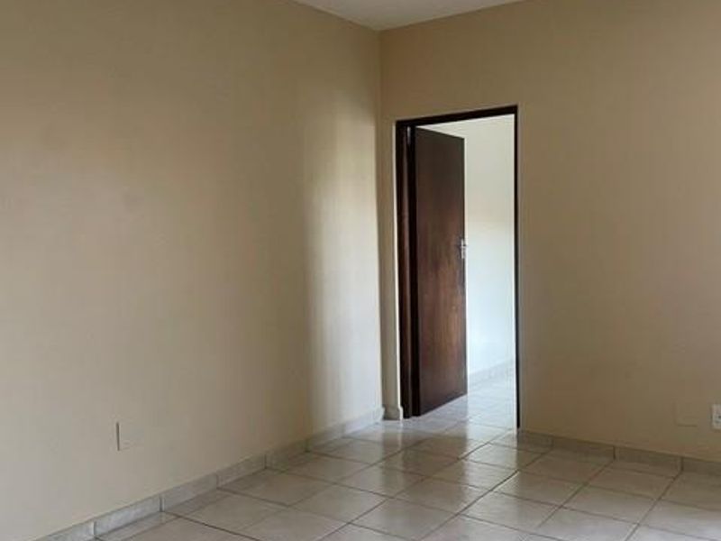 An empty bedroom featuring neutral wall paint, tiled flooring, and a timber door leading to an adjacent room.