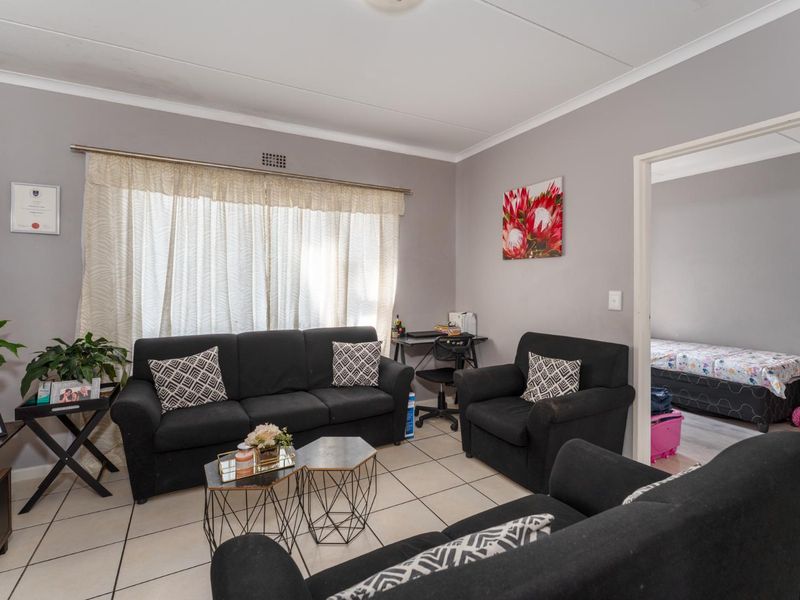 A comfortable living room featuring neutral grey walls, tiled flooring, and a coved ceiling, with direct access to an adjacent bedroom.