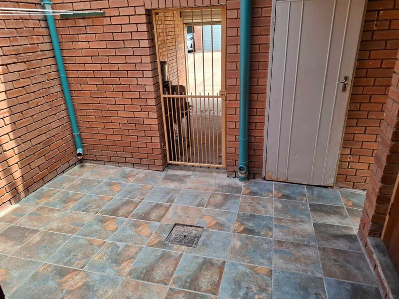 A functional outdoor utility or courtyard area featuring brick walls, tiled flooring, and a secure gated entrance.