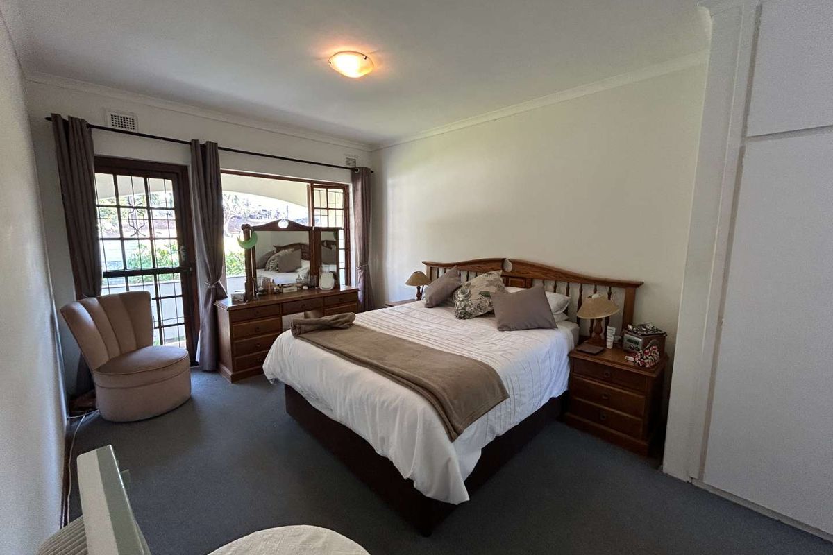 A spacious bedroom featuring built-in wardrobes, carpeted flooring, and direct access to an outdoor patio area through a glass-paned door.