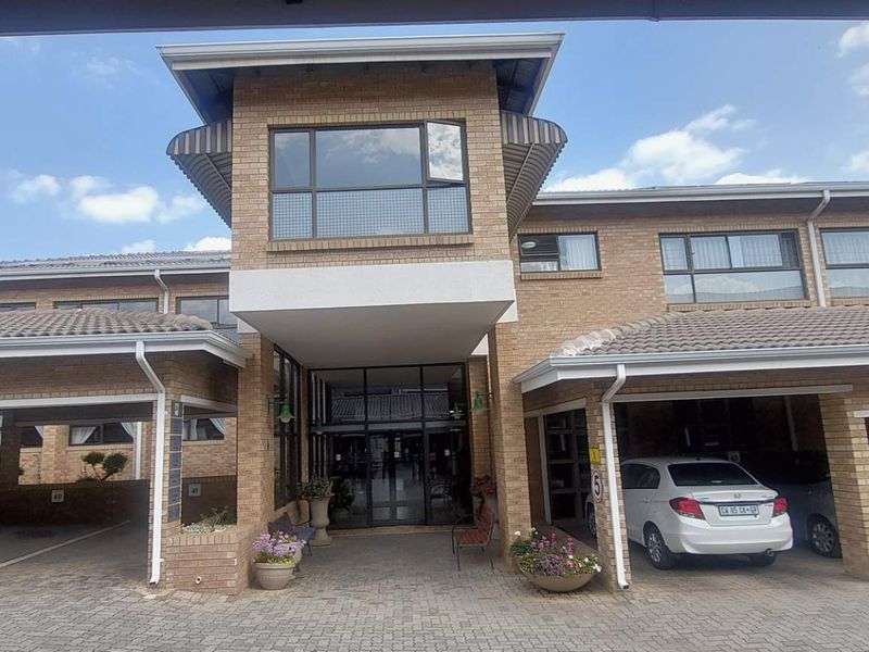 Front elevation of a retirement village building featuring a brick facade, covered parking bays, and a central glass entrance.
