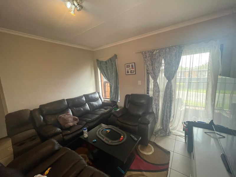A living room featuring tiled flooring, a sliding glass door with security gate, and neutral wall finishes.