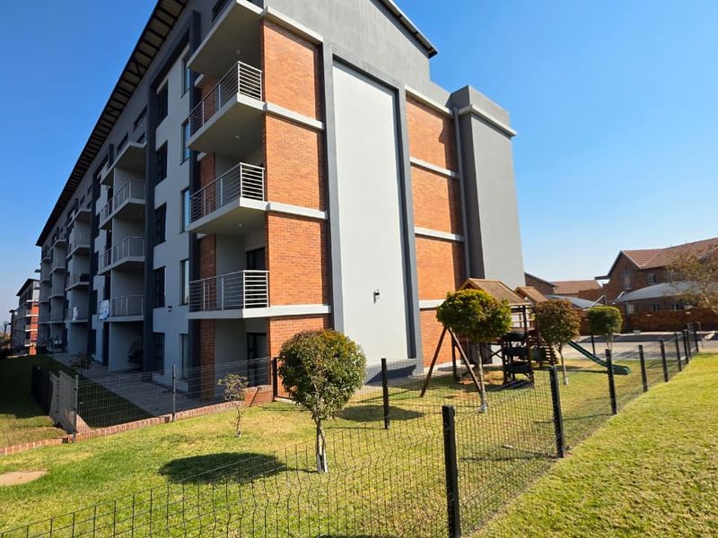 Exterior view of a modern apartment building featuring brick and plaster facade, private balconies, and a well-maintained communal garden area.