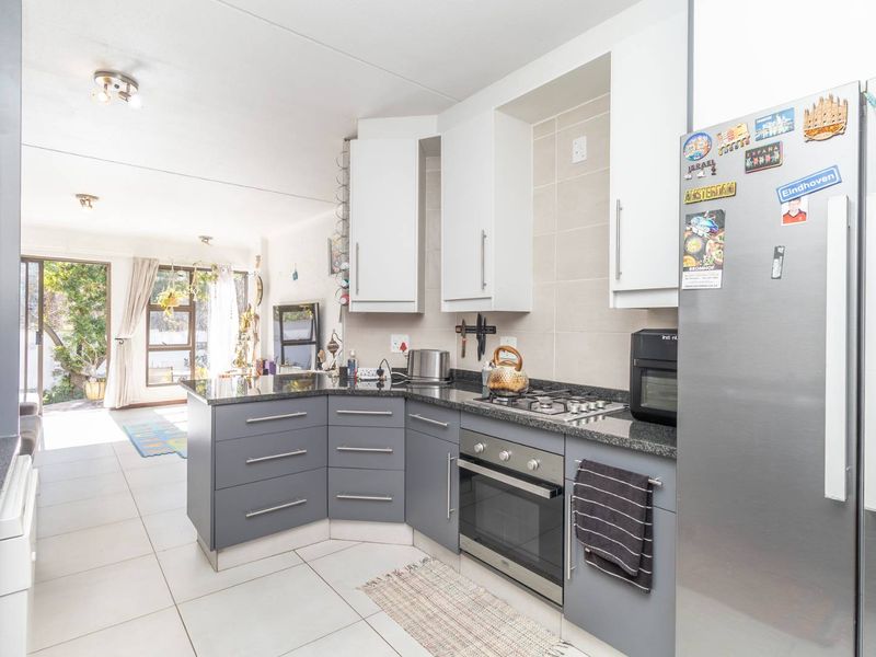 Modern open-plan kitchen featuring grey cabinetry, granite countertops, and integrated appliances, flowing seamlessly into a bright living area with access to the outdoors.