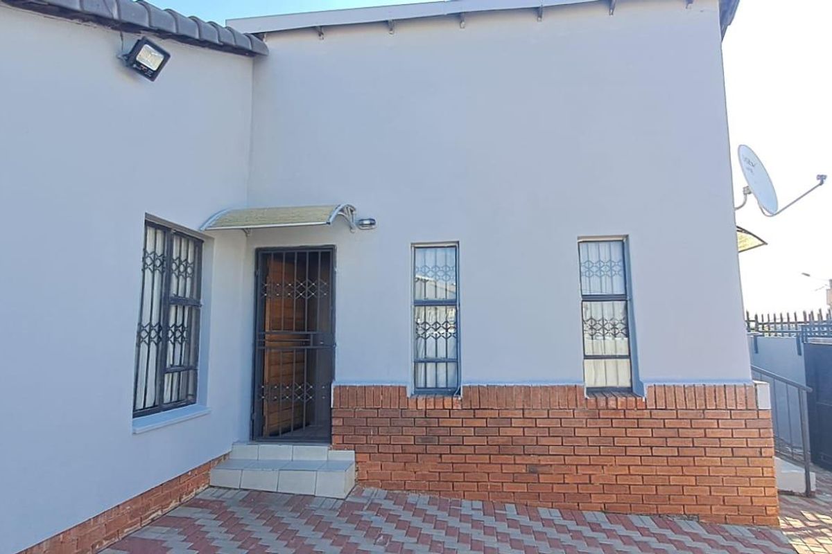 Rear exterior view of the house featuring a paved area, security gates, and brick facade detailing.