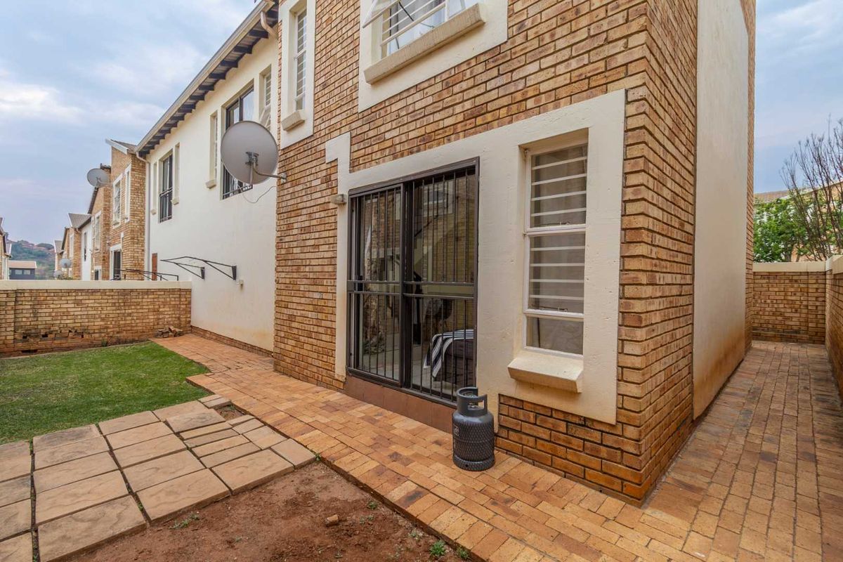 Rear exterior view of the townhouse featuring a face brick facade, paved patio area, and a small private garden space.