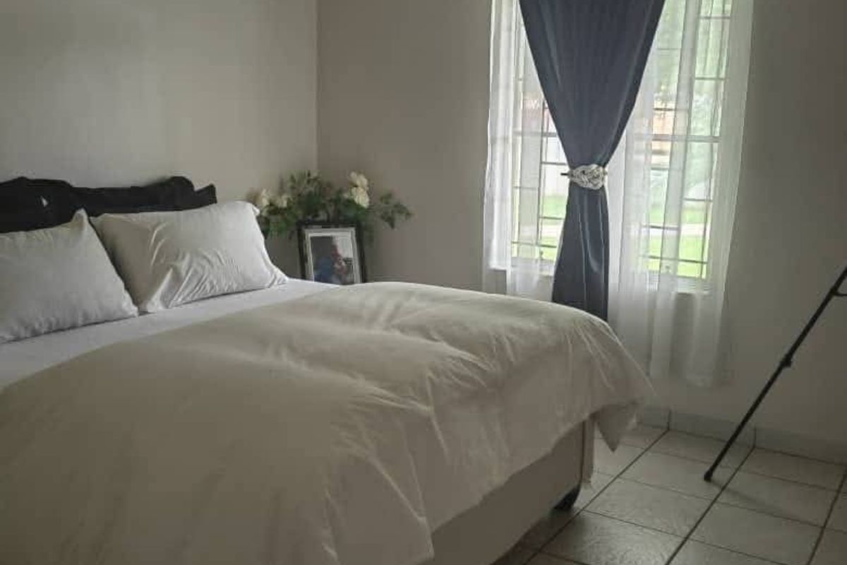 A bedroom featuring tiled flooring, an arched window with fitted curtain rod, and track lighting.