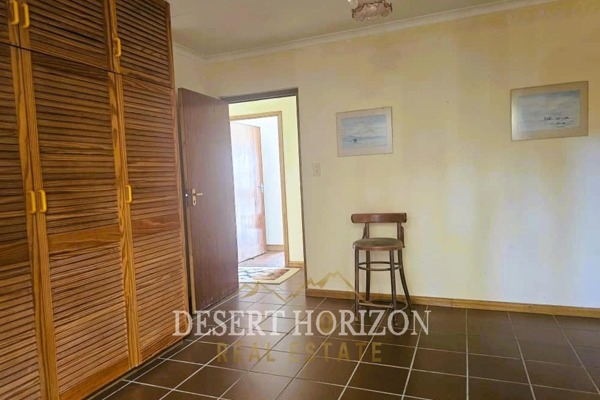 A bedroom featuring built-in wooden louvered wardrobes and tiled flooring, leading to an adjacent hallway.