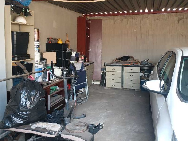 A functional garage space featuring a corrugated metal roof, concrete flooring, and built-in storage shelving, providing ample room for vehicle parking and utility storage.