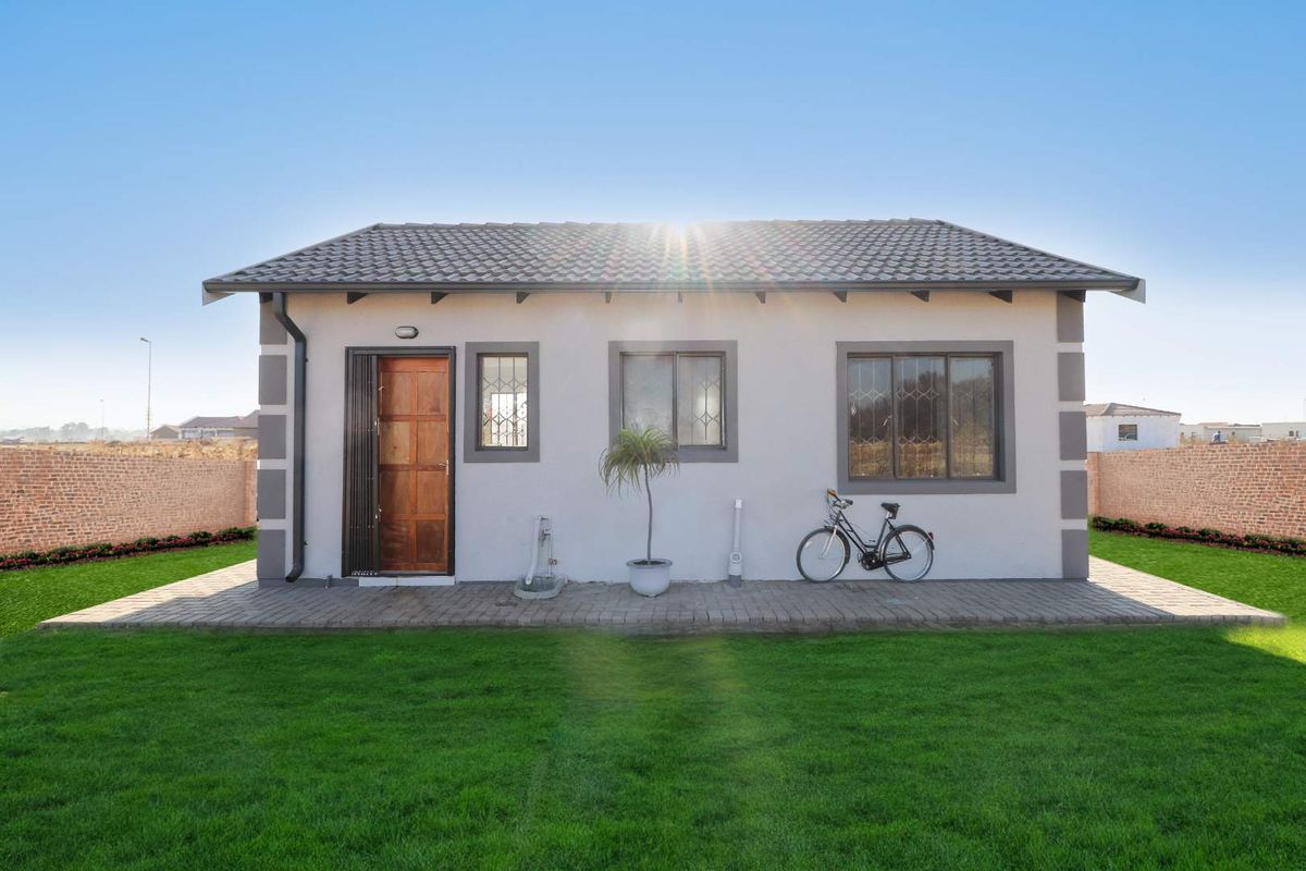 Rear view of a detached house featuring a paved patio, well-maintained lawn, and secure boundary walls.