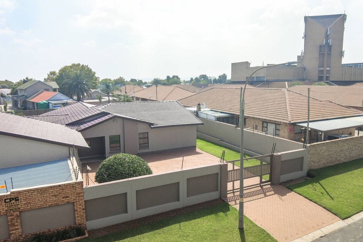 An elevated aerial view of the property showing the tiled roof, paved driveway, perimeter wall with electric fencing, and gated entrance.