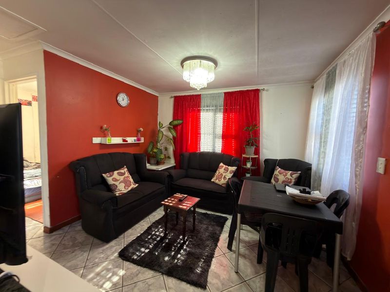 A living room featuring tiled flooring and a central ceiling light fixture, currently furnished with a seating area and dining space.