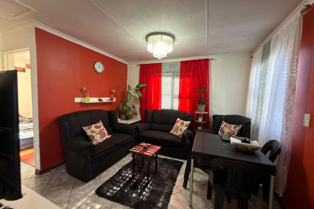 A living room featuring tiled flooring and a central ceiling light fixture, currently furnished with a seating area and dining space.