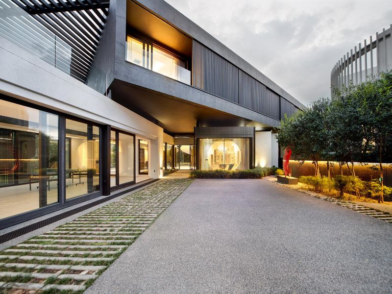 Modern architectural rear exterior featuring a concrete driveway, expansive sliding glass doors, and integrated lighting, showcasing a contemporary design aesthetic.