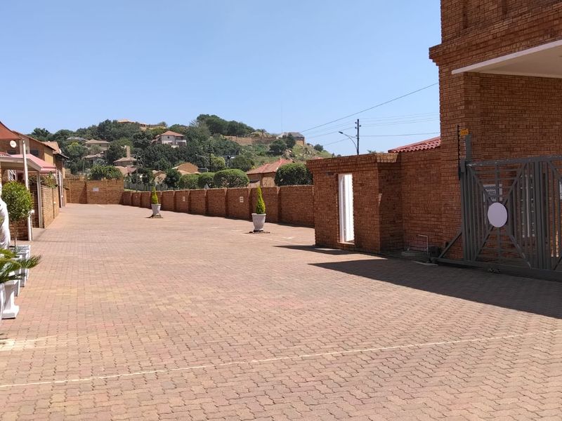 A secure townhouse complex entrance featuring a paved driveway, brick boundary walls, and a sliding security gate.