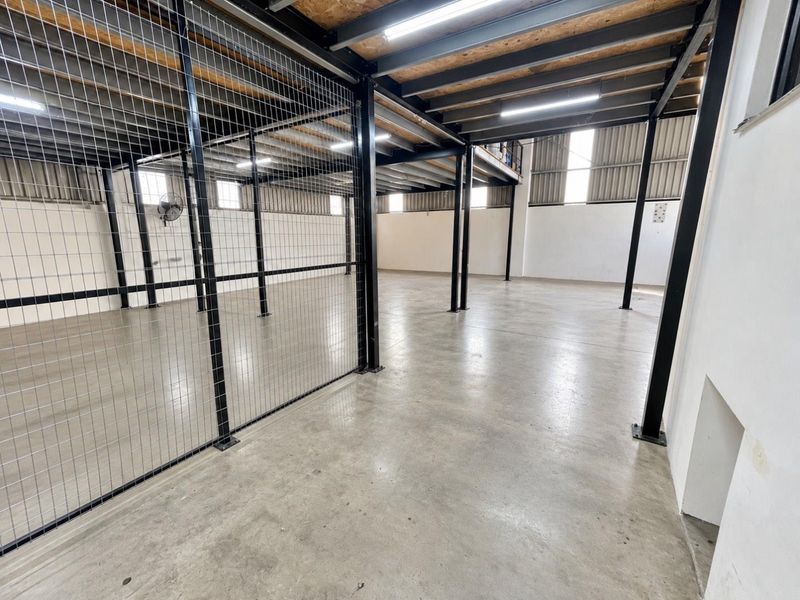 Spacious industrial utility area featuring concrete flooring, a steel mezzanine level, and secure wire mesh partitioning, suitable for storage or workshop use.