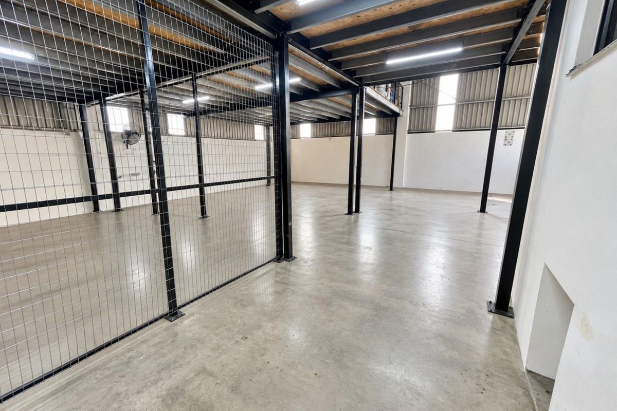 Spacious industrial utility area featuring concrete flooring, a steel mezzanine level, and secure wire mesh partitioning, suitable for storage or workshop use.