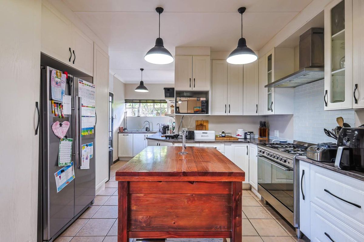 A functional kitchen featuring white cabinetry, a central wooden island, stainless steel gas stove, extractor fan, and tiled flooring.