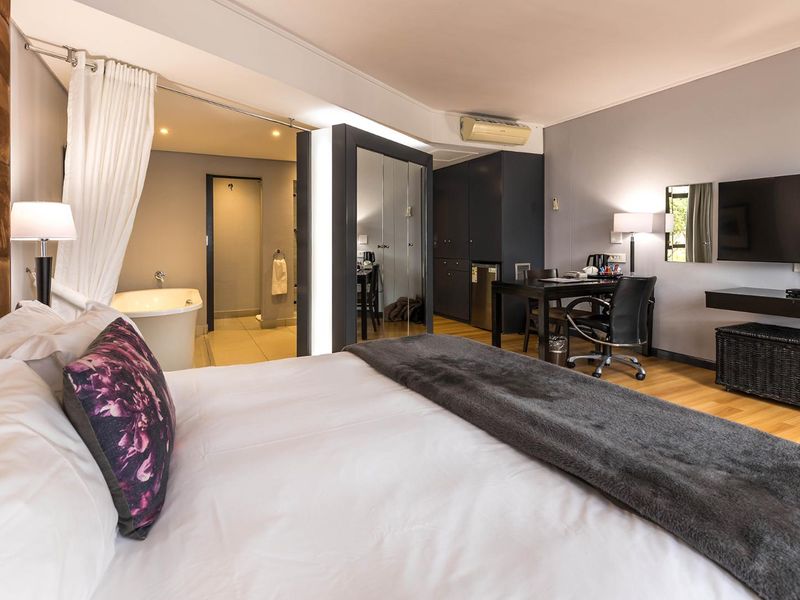 Modern bedroom featuring laminate flooring, built-in wardrobe, split-system air conditioning, and an open-plan ensuite area with a freestanding bathtub.