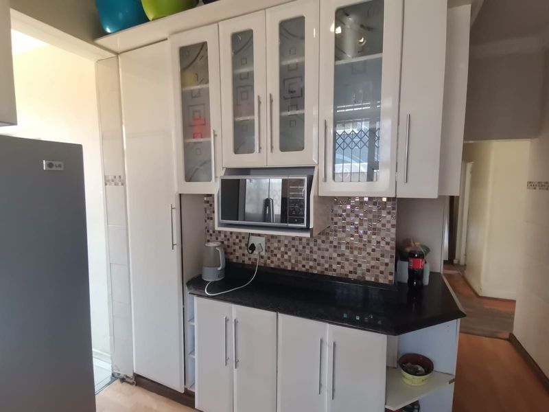 A functional kitchen area featuring white cabinetry, a dark granite countertop, and a decorative mosaic tile backsplash with a built-in microwave.