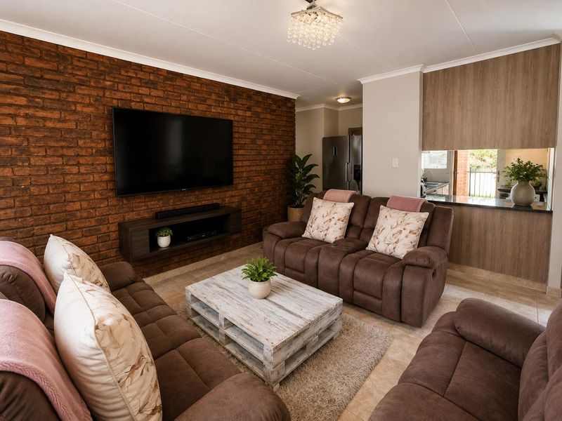 Open plan living area featuring an exposed brick wall, tiled flooring, and a modern kitchen with granite countertops and wood-finish cabinetry.
