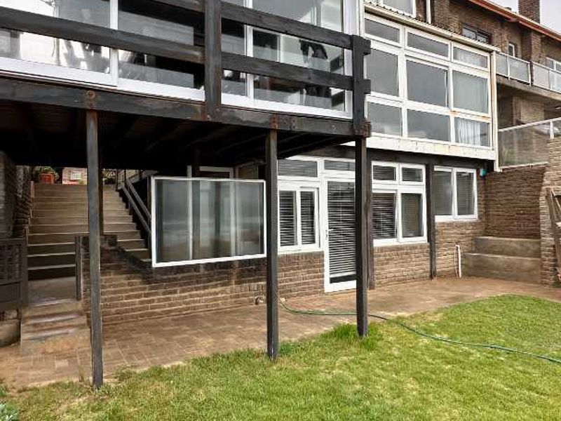 Rear view of the townhouse featuring a raised timber deck, paved patio area, and a private lawn with brick exterior finishes.