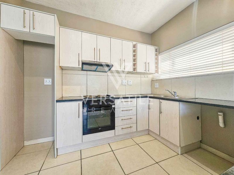 A clean and functional kitchen featuring light-toned built-in cabinetry, dark countertops, a built-in oven with extractor fan, and tiled flooring throughout.
