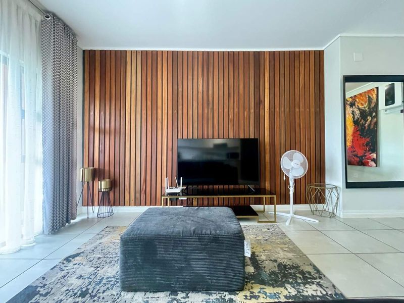 A modern living room featuring a warm timber slat feature wall, neutral tiled flooring, and large sliding glass doors providing natural light.