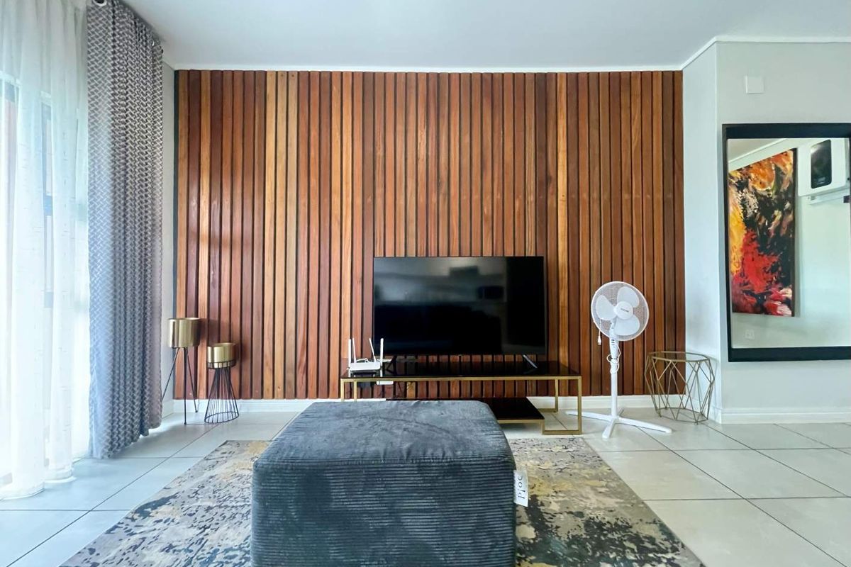 A modern living room featuring a warm timber slat feature wall, neutral tiled flooring, and large sliding glass doors providing natural light.