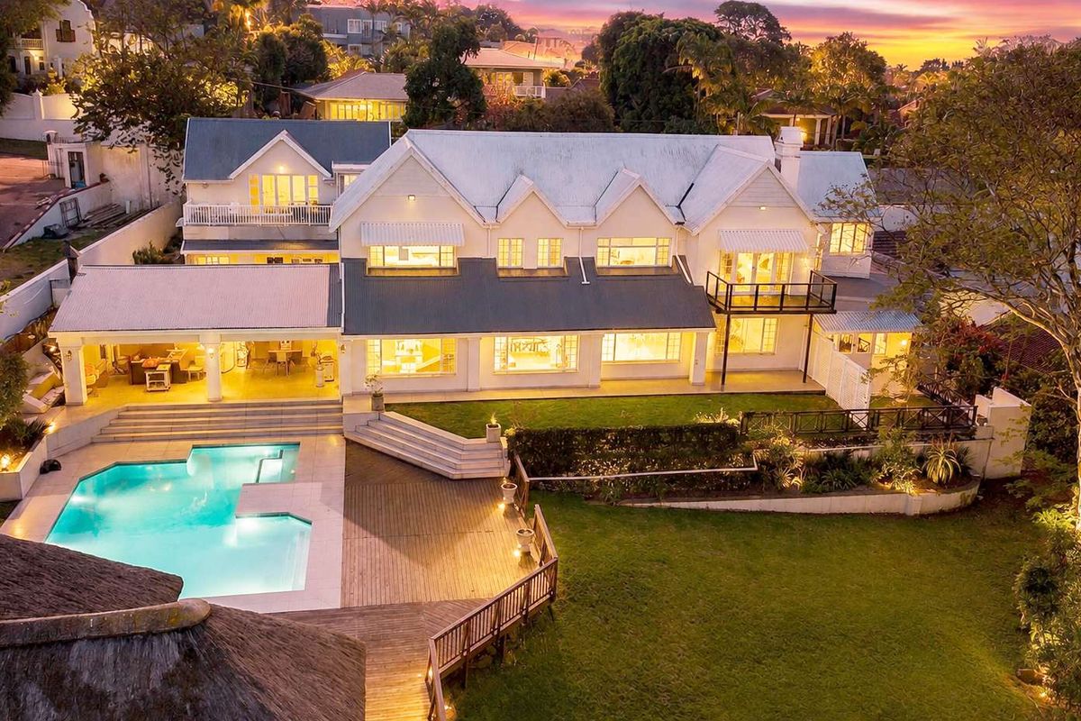 Stunning aerial view of a large residential property featuring a swimming pool, expansive timber decking, covered patio, and well-maintained landscaped gardens at dusk.