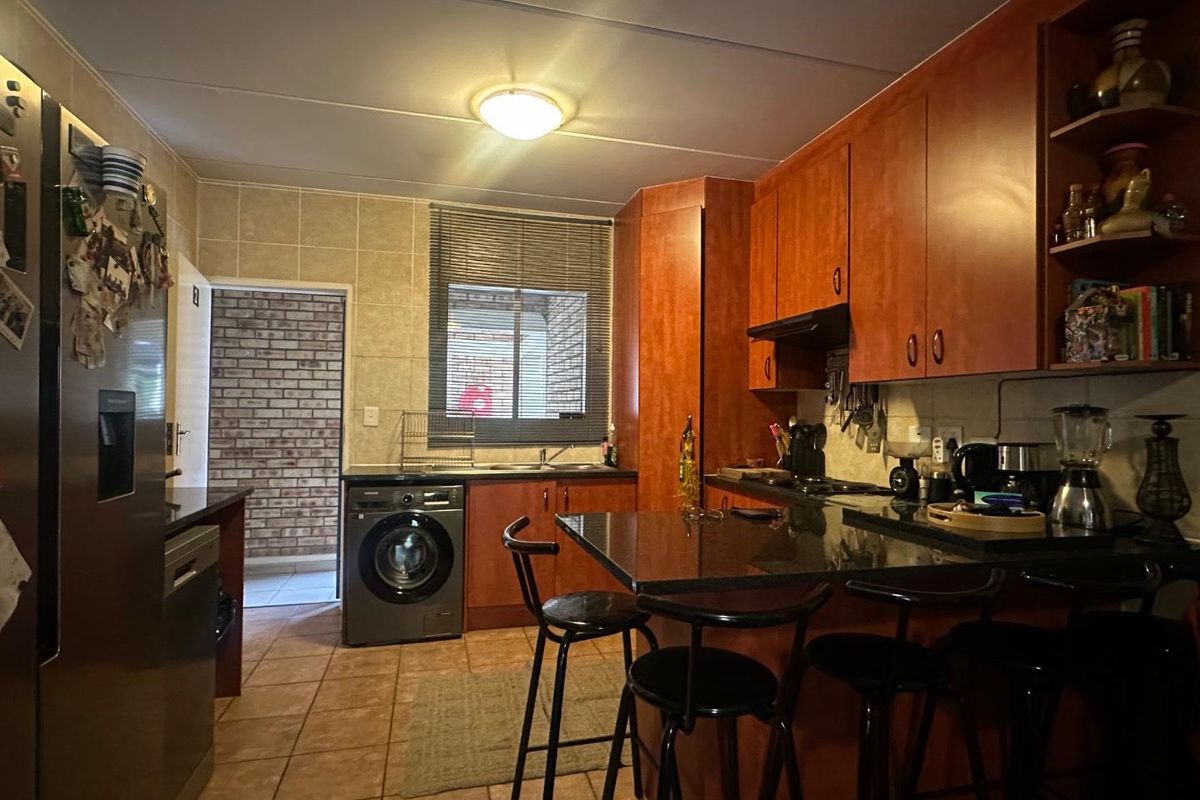 A functional kitchen featuring wood-toned cabinetry, granite countertops, a breakfast bar, and integrated laundry facilities, with direct access to an exterior area.