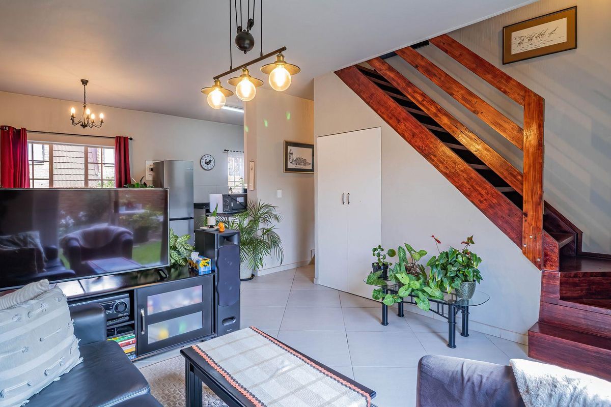 A well-lit living room featuring tiled flooring, a prominent wooden staircase, and integrated storage, creating a functional and inviting open-plan living space.