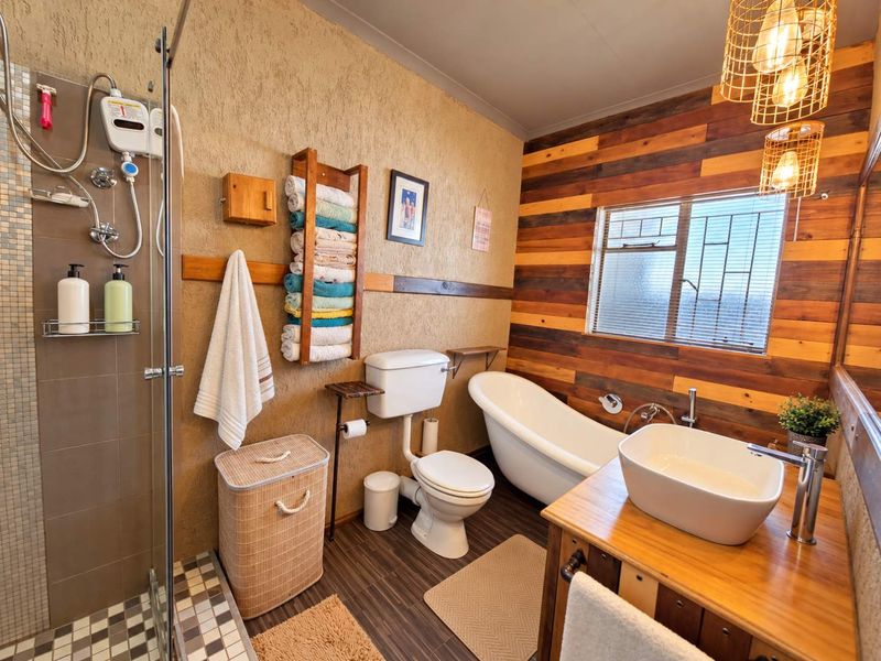 A rustic-style bathroom featuring a freestanding bathtub, glass-enclosed shower, vessel sink on a wooden vanity, and distinctive timber wall paneling.