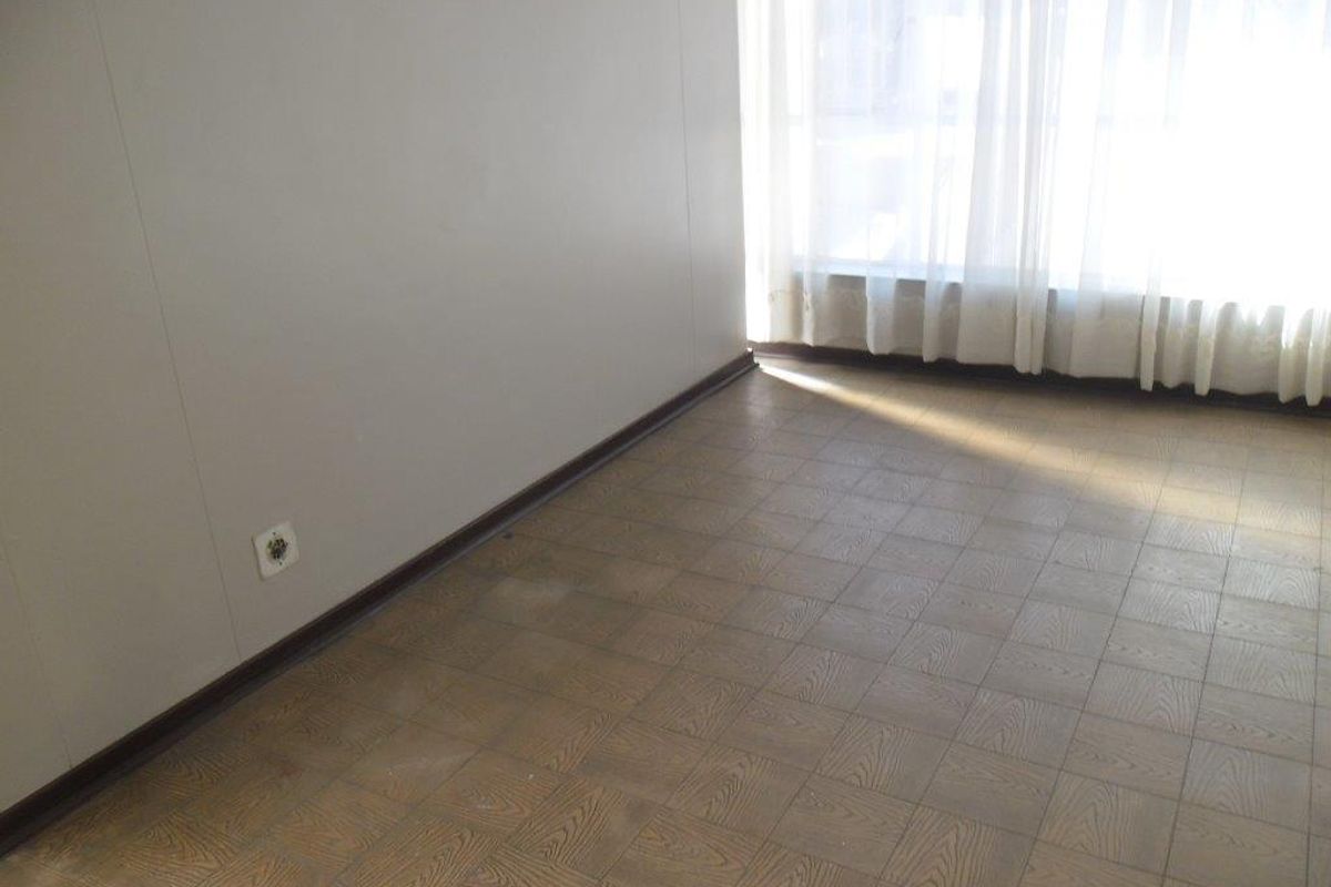 An empty bedroom featuring parquet flooring and a large window with curtains, offering a blank canvas for renovation or interior design updates.