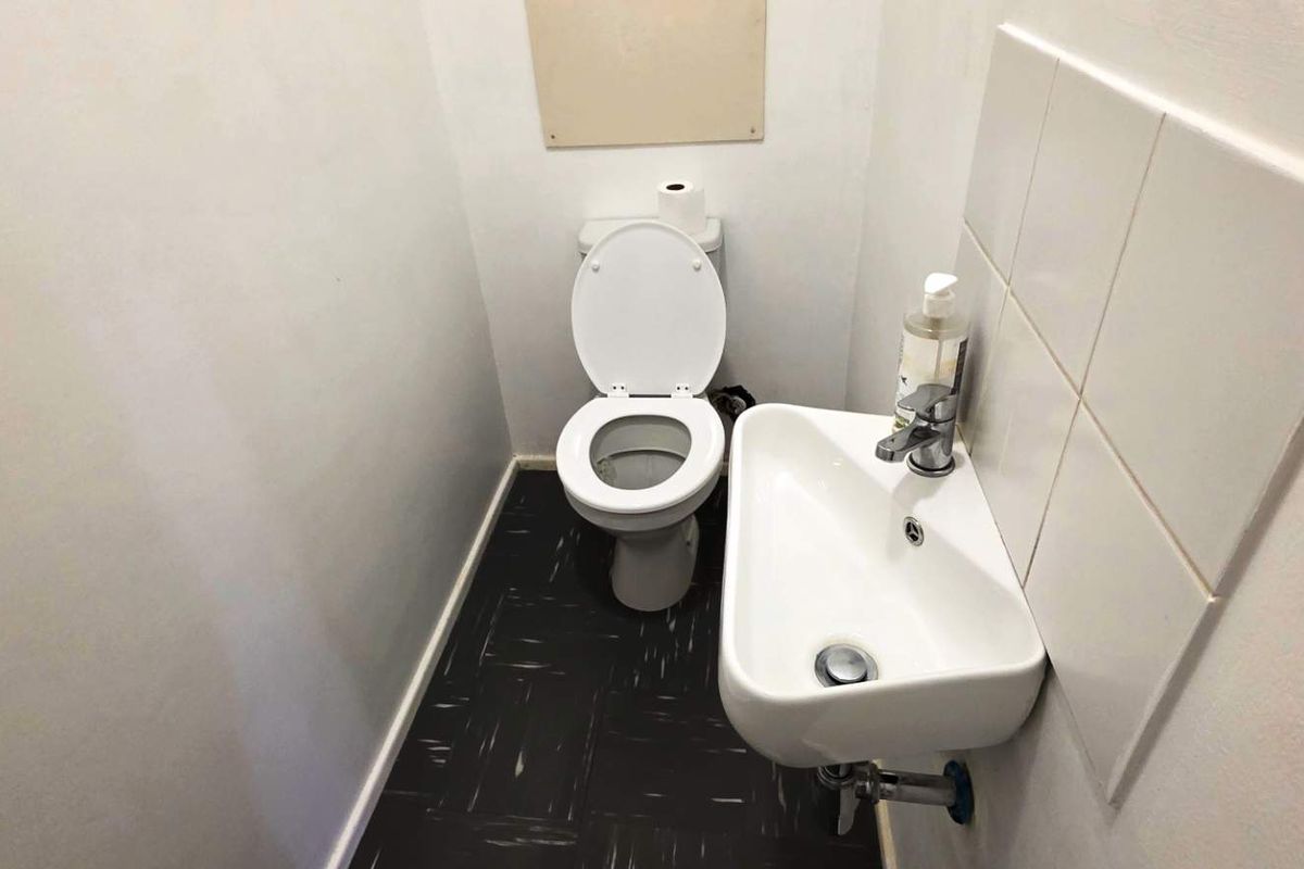 A compact office restroom featuring a wall-mounted basin with chrome mixer, tiled splashback, and a standard toilet.