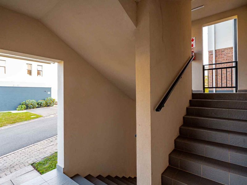 A clean, well-maintained stairwell area featuring tiled steps, a secure handrail, and a wall-mounted fire extinguisher, providing access to the apartment complex.