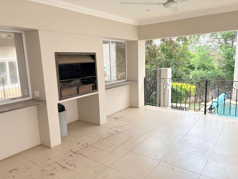 Covered patio featuring a built-in braai, ceiling fan, and wrought iron balustrade overlooking the garden and pool area.