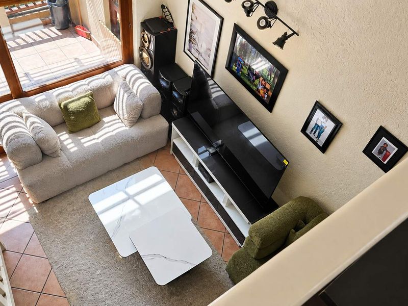 A bright living room featuring tiled flooring, track lighting, and a large sliding glass door providing access to an outdoor patio area.