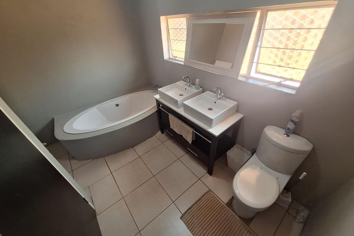 A functional bathroom featuring a built-in corner bathtub, a double vanity with dual vessel sinks, and a standard toilet.